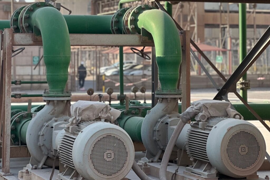 Two centrifugal pumps driven by electric motors with dust covers, connected to large green flanged pipework in an industrial plant