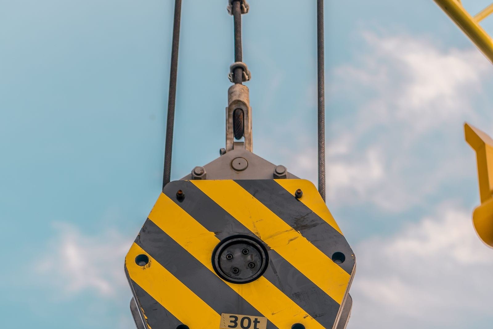 Yellow and black striped crane hook block marked 30t hanging on its wire ropes against a blue sky