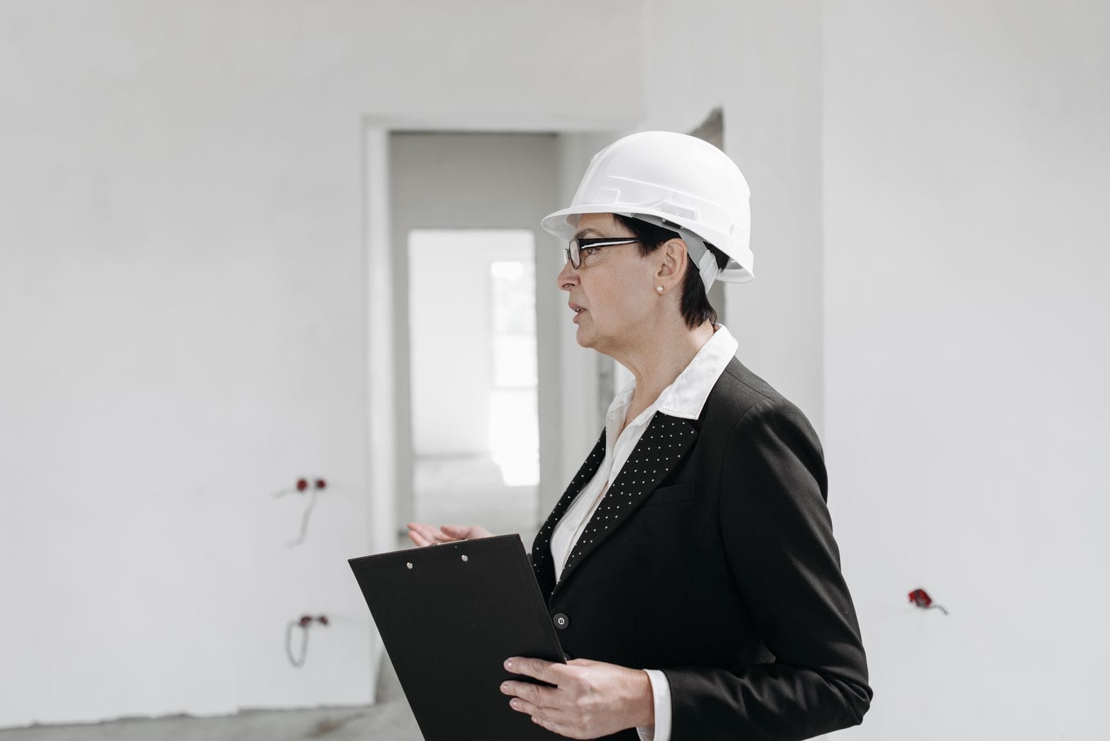 Woman in a white hard hat and dark blazer holding a clipboard while assessing a site