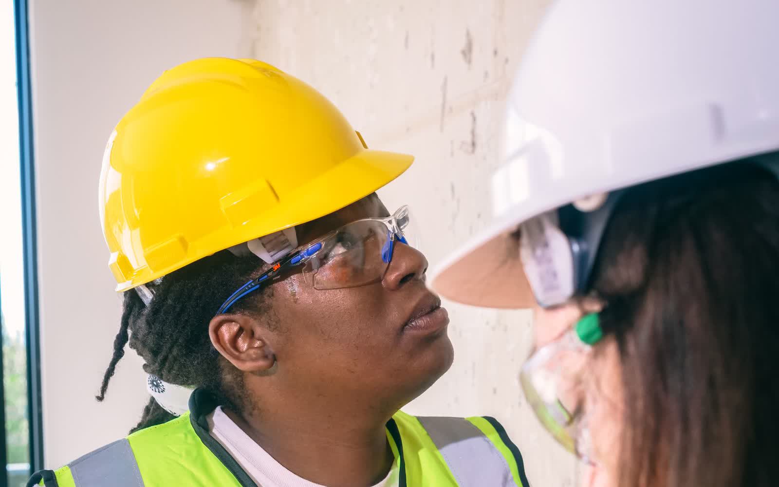 Two inspectors in hard hats, safety glasses and high-visibility vests looking up at equipment during a site inspection