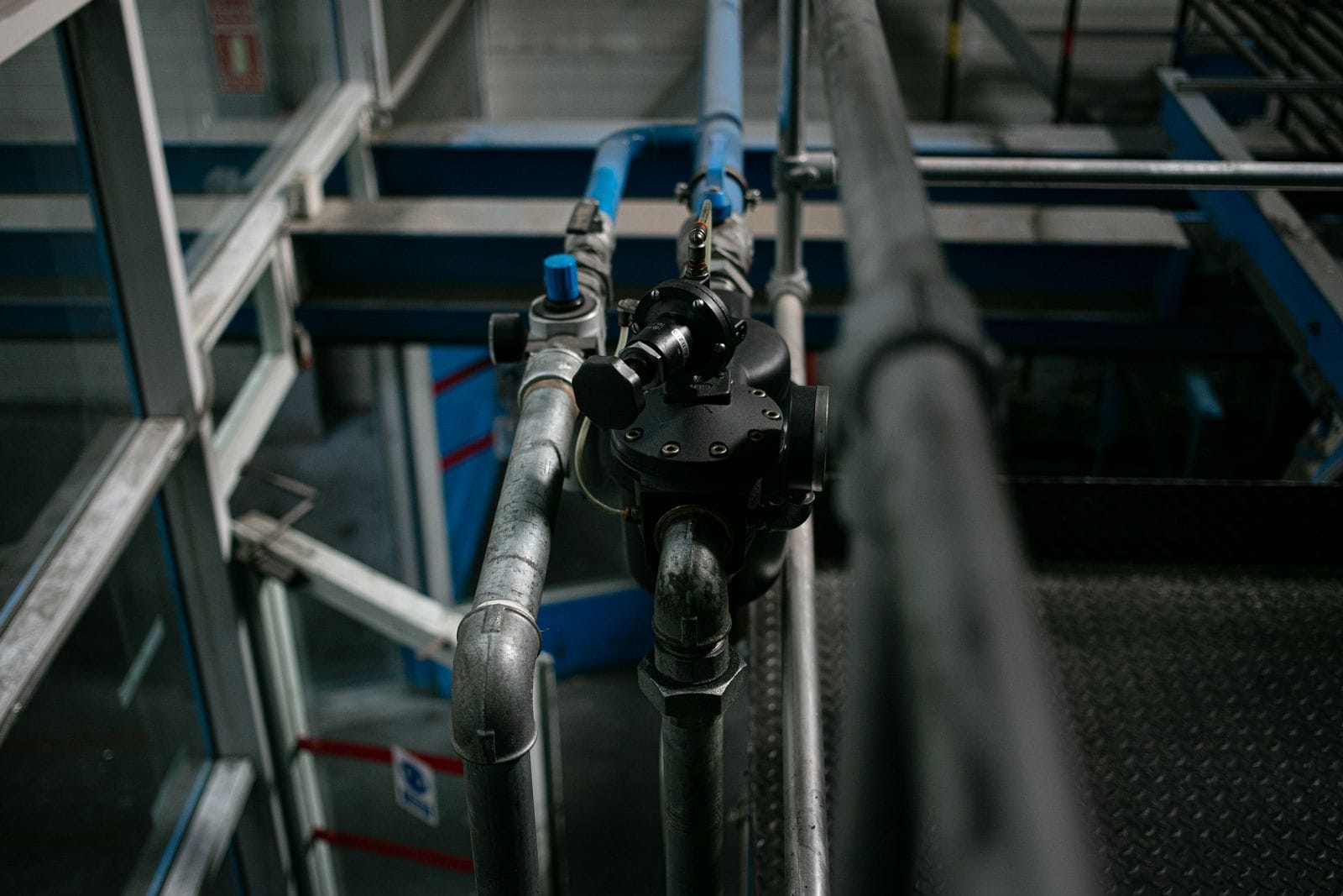 Close view of a steel pipe run with a black valve and blue lines beside an industrial stairway